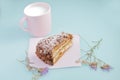 Slice of cake with icing on duck egg blue background with dried flowers and pink cup of milk