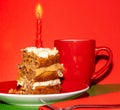 Slice of carrot cake with lighted red candle on red background, red cup and fork, square