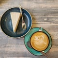 a slice of cheesecake on a dessert plate with a fork and a cup of cappuccino coffee with foam Royalty Free Stock Photo