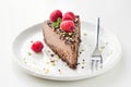 Slice of chocolate cake cheesecake decorated with crushed pistachio nuts, raspberries and mint leaf