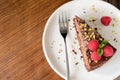 Slice of chocolate cake topped with raspberries, pistachio nut and mint leaf on white plate. Royalty Free Stock Photo