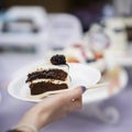 Slice of delicious chocolate cake with cream and blackberries, plate in hand, fresh summer dessert, selective focus