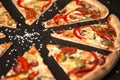 Slice of delicious pizza with vegetables and meat on dark board. Sea salt on background Royalty Free Stock Photo