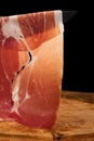 Slice of dry cured ham, on wood and black backdrop Royalty Free Stock Photo