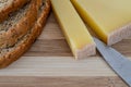 Slice of french comte cheese on wood cutting board with sliced 7-grain bread