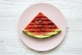 Slice of fresh ripe grilled watermelon on round pink plate over white wooden background, top view. Royalty Free Stock Photo