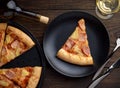 Slice of hawaiian pizza on black plate with glass of wine, cutlery and bottle on wooden table. Royalty Free Stock Photo