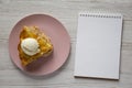 Slice of homemade apple pie with ice cream on a pink plate, blank notepad over white wooden background, top view Royalty Free Stock Photo