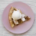 Slice of homemade apple pie with ice cream on pink plate over white wooden surface, overhead view. Flat lay Royalty Free Stock Photo