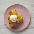 Slice of homemade apple pie with ice cream on a pink plate over white wooden surface, overhead view Royalty Free Stock Photo