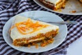 A slice of homemade carrot cake with cream and a white and brown checkered towel on a white kitchen table. Vegan and Gluten Free Royalty Free Stock Photo