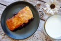 Slice of homemade cherry pie on the black plate, glass of milk and white flower on the light wooden table Royalty Free Stock Photo