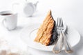 A slice of homemade multilayer biscuit cake. Soaked in butter. Served with chocolate icing and coconut. On a white plate is a fork Royalty Free Stock Photo