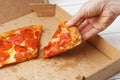 Slice of italian pepperoni pizza in hand and open box with pizza leftovers Royalty Free Stock Photo