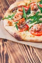 slice of italian pizza with royal prawns, tomatoes, cheese and arugula on a classic dough on a wooden table