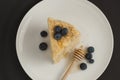 Slice of layered homemade honey cake selective focus bluebery white round plate black background top view