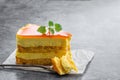 Slice of layered mango cheesecake on gray background