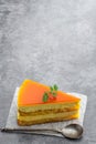 Slice of layered mango cheesecake on gray background