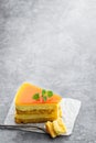 Slice of layered mango cheesecake on gray background