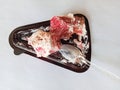 a slice of layered red bread covered in white cream with a platebrown triangle and transparent plastic spoon