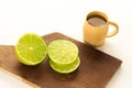 Slice lemon or lime in a wood board and a shot of cachaÃÂ§a, in a white background.