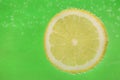 Slice of lemon in sparkling water on green background, space for text. Citrus soda Royalty Free Stock Photo