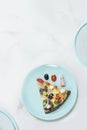 Slice of meat pizza with vegetables on turquoise sering plate with ingredients^ black olive, bacon, cherry tomato o