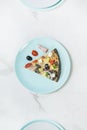 Slice of meat pizza with vegetables on turquoise sering plate with ingredients^ black olive, bacon, cherry tomato o