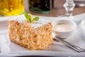 Slice of Napoleon cake close-up on white dish with mint leaf and bowl of cream sauce