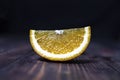 A slice of orange lies on a wooden surface on a dark background