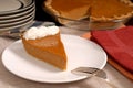 Slice of pumpkin pie with extra plates resting in background along with remaining pie