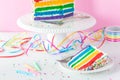 A slice of rainbow birthday cake with the rest of the cake on a stand in behind. Royalty Free Stock Photo