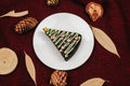 Slice of sweet chocolate cake for Christmas Eve in shape of Christmas Trees with green icing and festive sprinkles on white plate. Royalty Free Stock Photo