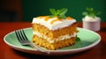 Slice of tasty sweet carrot sponge cake with cream decorated with mint leaf served on plate with spoon on table on colorful