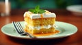 Slice of tasty sweet carrot sponge cake with cream decorated with mint leaf served on plate with spoon on table on colorful