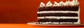 Slice of three-layer chocolate cake with white frosting and meringue ghosts on an orange background. Royalty Free Stock Photo