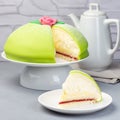 Slice of traditional Swedish dessert Princess cake with green marzipan cover and pink rose decoration, on gray background, square