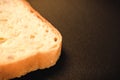 slice of white bread close up on a black background. rough dappled textured surface chopped piece loaf of natural organic food wit