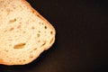 slice of white bread close up on a black background. rough dappled textured surface chopped piece loaf of natural organic food wit