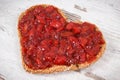 Slice of bread in shape of heart with strawberry jam for breakfast. Rustic background Royalty Free Stock Photo