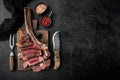 Sliced barbecued tomahawk rib tip with rosemary, salt and herbs medium rare, on wooden serving board, on black stone background, Royalty Free Stock Photo