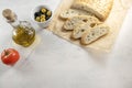 Sliced bread on baking paper with olives, tomato and olive oil on a white table with place for text. Fresh, tasty focaccia serving Royalty Free Stock Photo