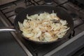 Sliced brown onions frying in a saucepan on a gas oven