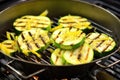 sliced courgettes in a grill basket over barbecue flames