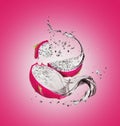 Sliced dragon fruit with splashes of juice on a pink background