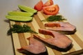 Sliced fish with cucumber and tomato and dill on a wooden board.