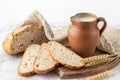 Sliced fresh baked spelt wheat loaf of bread, clay rural jug of milk on wooden cutting board, rustic linen towel and spikelets on