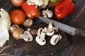 Sliced fresh mushrooms on a dark Board with a knife, ripe red tomato, bell pepper, lettuce leaves on a wooden background Royalty Free Stock Photo