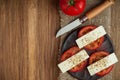 Sliced ??fresh tomatoes under cheese with mediterranean spices on a clay plate on a burlap napkin on an old wooden surface. Royalty Free Stock Photo