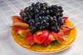 Sliced fruit - apples, oranges, kiwi topped with grapes on white dish Royalty Free Stock Photo